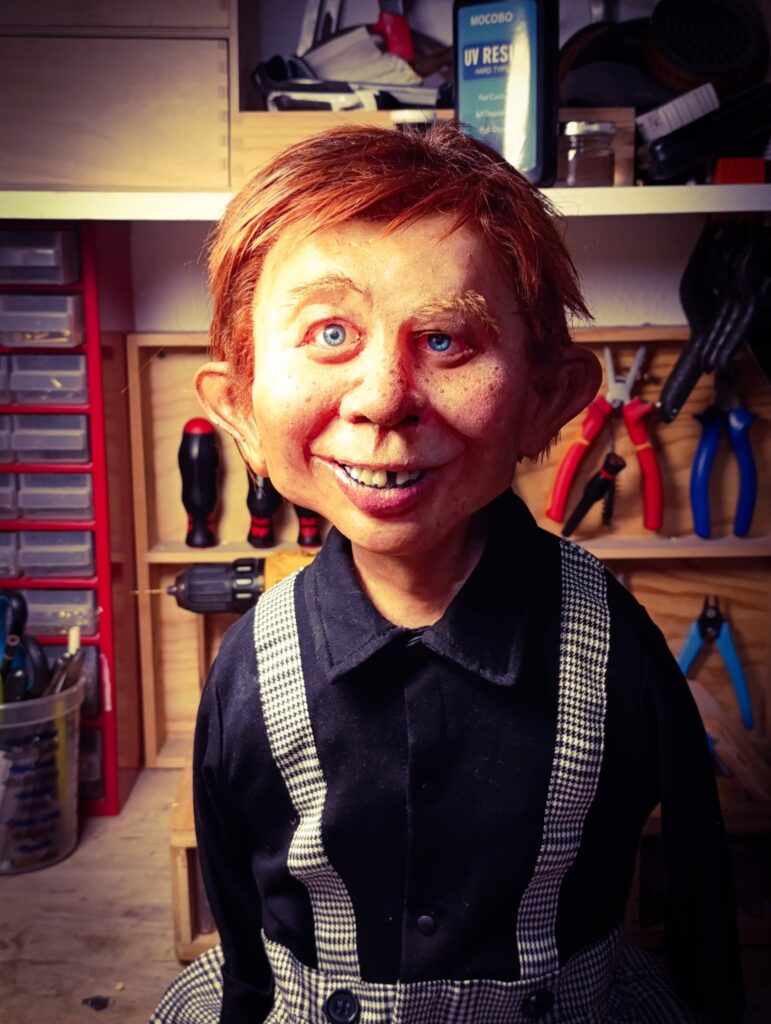 A nearly completed Alfred E. Neuman bust by Pierre Schrader, featuring hand-punched reddish-brown hair, detailed skin texture, a black shirt, and houndstooth suspenders.